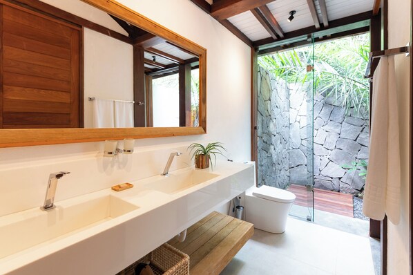 A modern bathroom with a large mirror, two sinks, a toilet, and a shower area.
