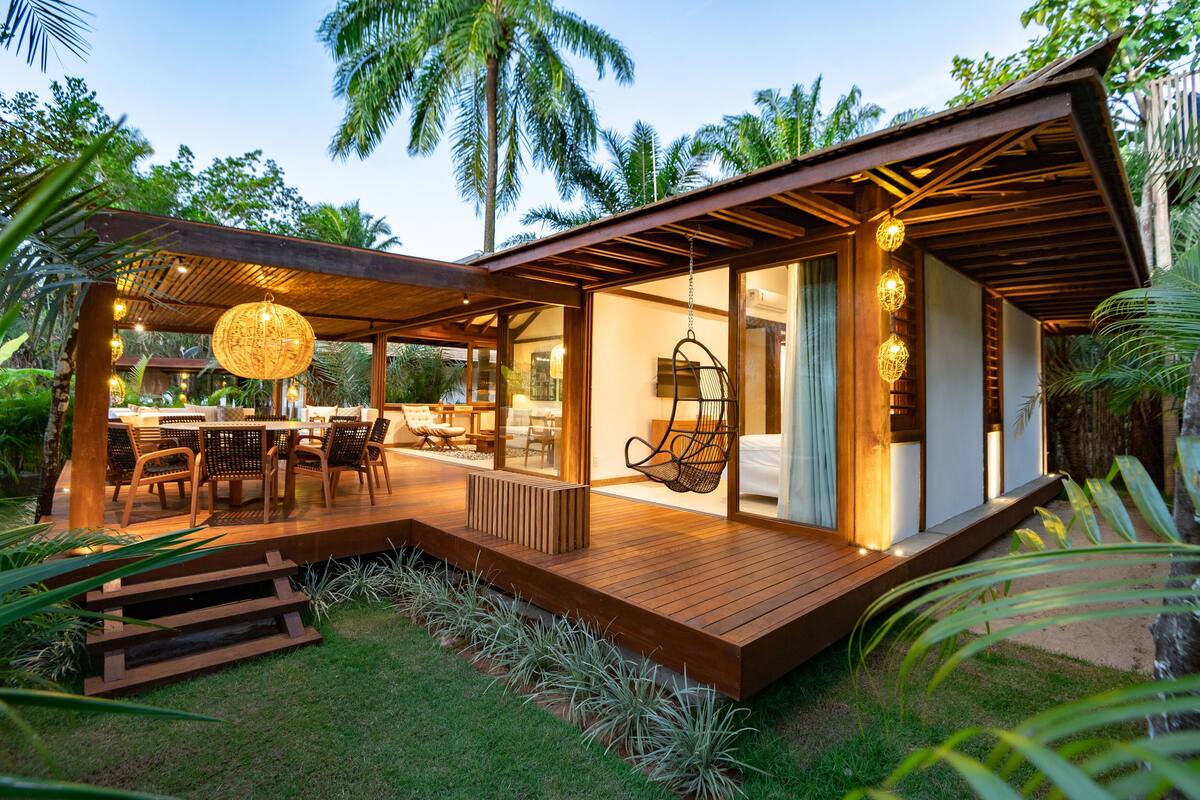 A modern outdoor dining area with a wooden deck, seating, and hanging lights.