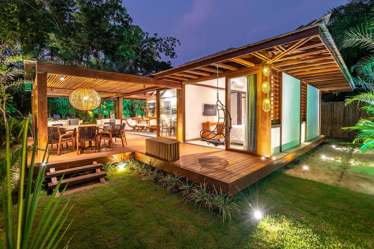 A modern outdoor patio with wooden flooring, a dining area with chairs, and a hanging light fixture.