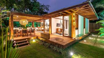 A modern outdoor patio with wooden flooring, a dining area with chairs, and a hanging light fixture.