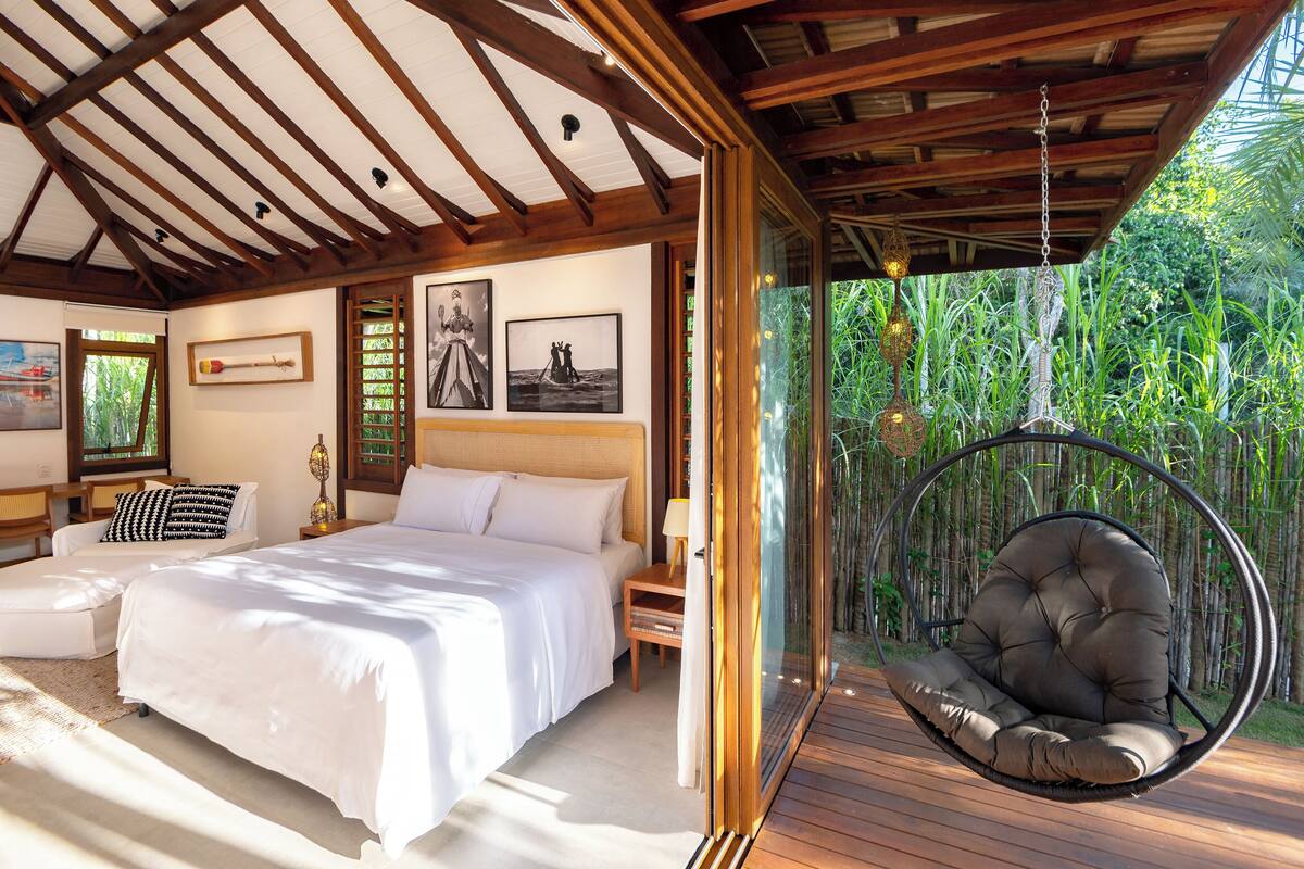 A bedroom with a large bed, a hanging chair, and a view of a bamboo forest.