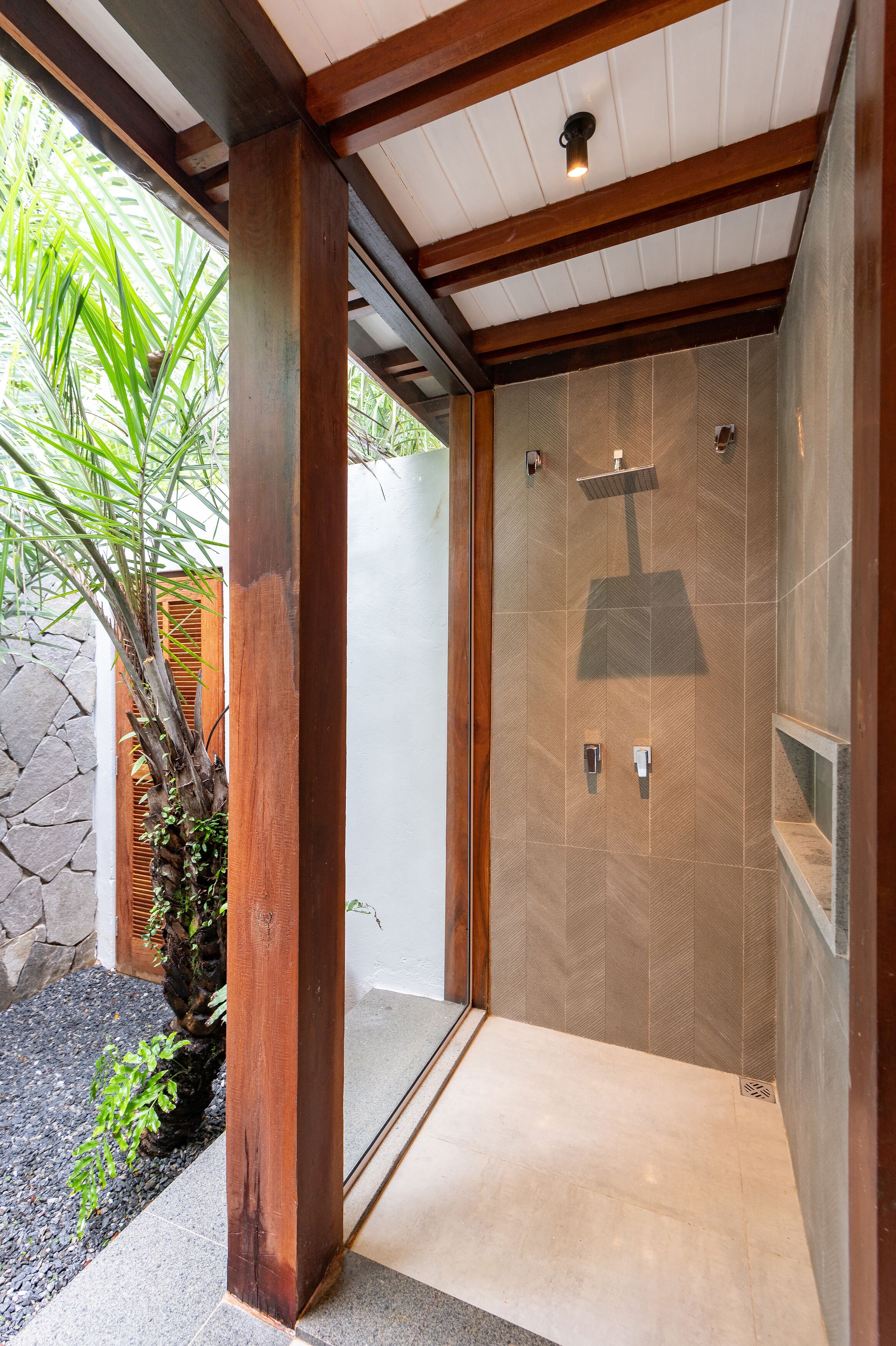 A modern shower with a glass door, wooden beams, and a stone wall in the background.