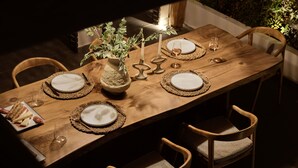 Een houten eettafel gedekt met borden, glazen en een kaars.
