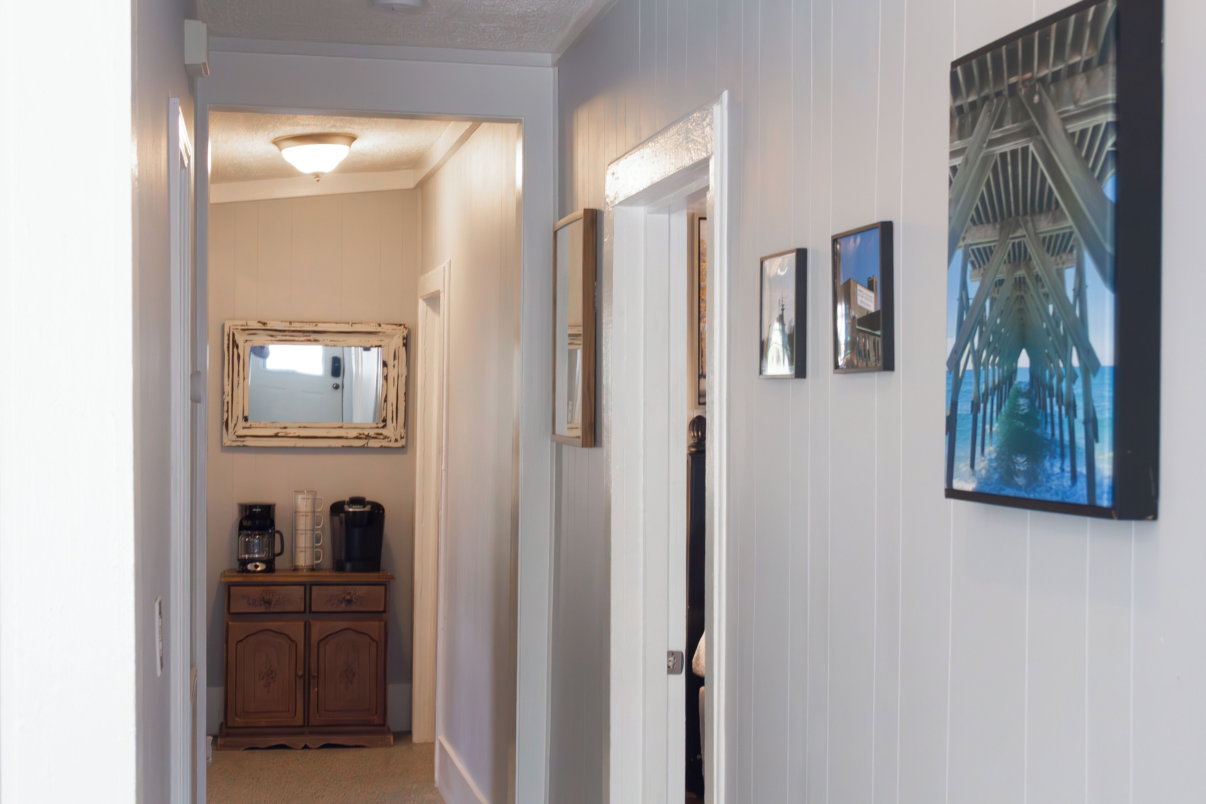 Un couloir avec une armoire en bois, un miroir et des tableaux encadrés accrochés au mur.