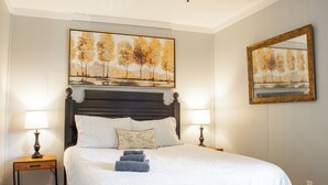 Een net opgemaakt bed met een witte dekbedovertrek en kussens, twee nachtkastjes met lampen, en een schilderij boven het bed.
