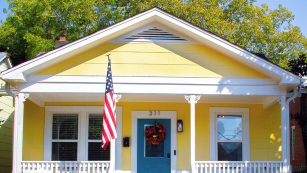 Een geel huis met een blauwe deur, witte veranda-leuningen en een Amerikaanse vlag.