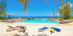 A beach with clear turquoise water, lounge chairs, and kayaks.
