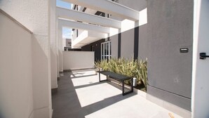Een moderne buitenruimte met een bank en planten, gekenmerkt door een strak, minimalistisch design met witte muren en een grijze vloer.