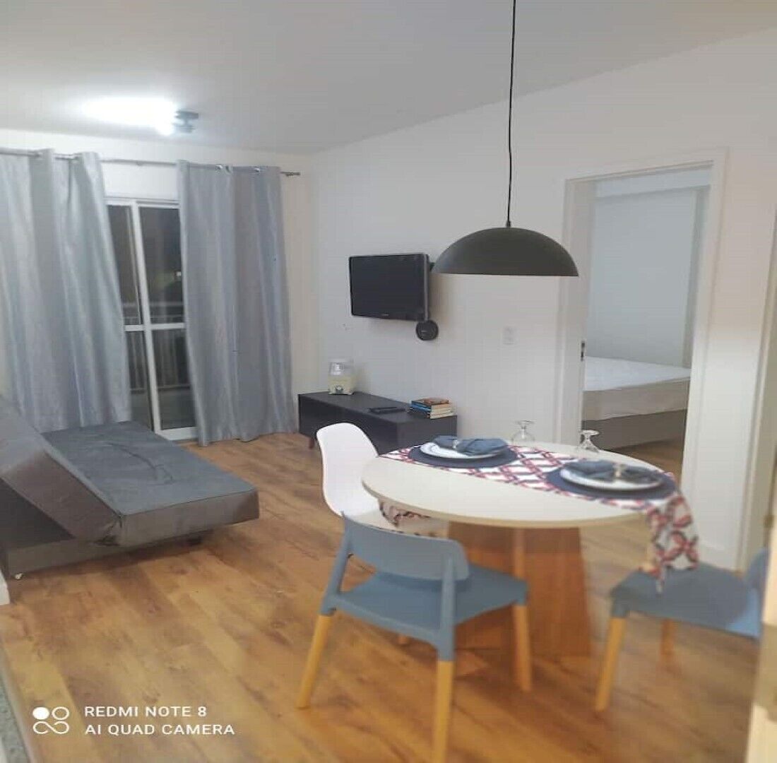 A compact living space with a dining table, chairs, a sofa, a TV, and a bed.