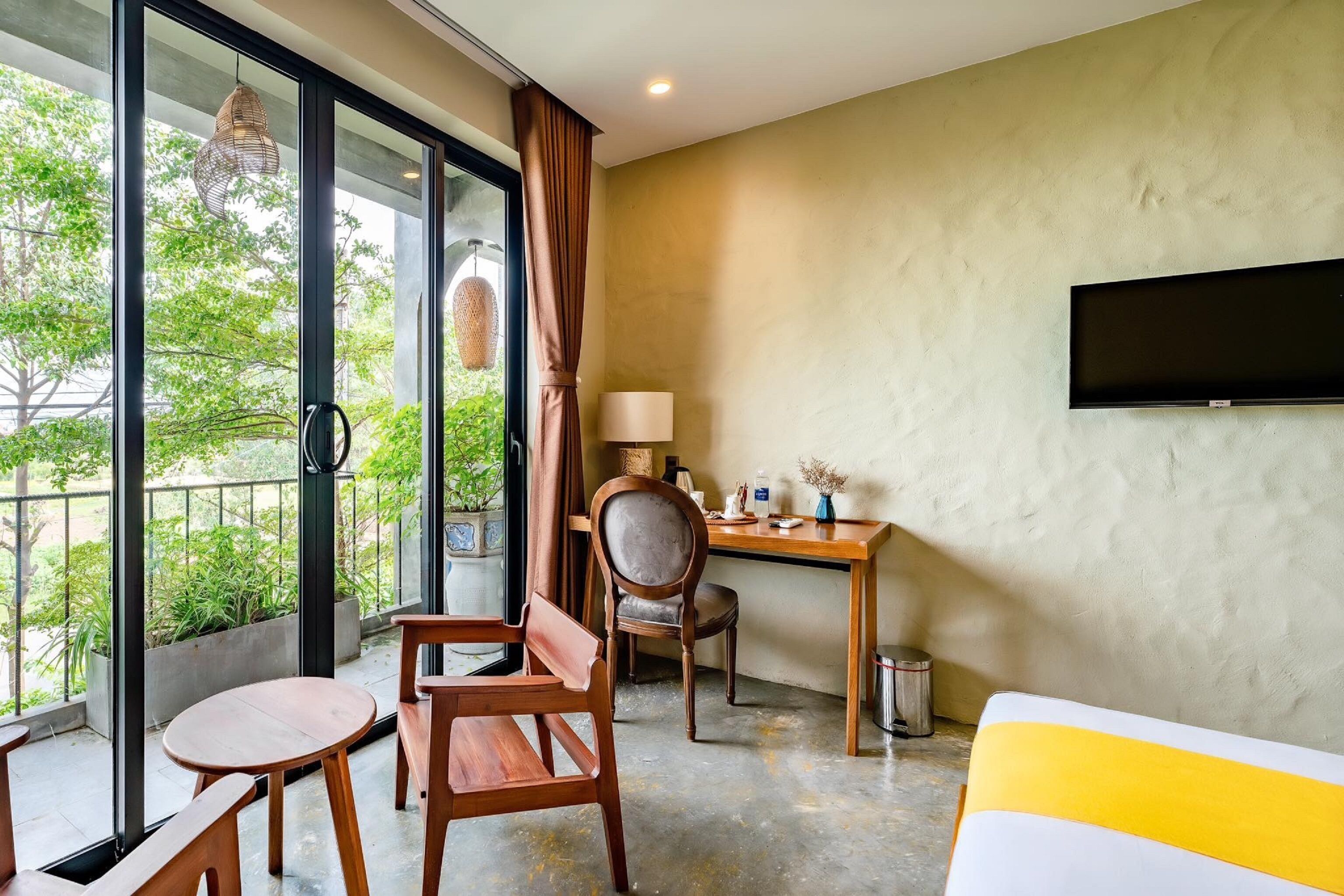 A hotel room with a large window, a desk, a chair, a bed, and a TV mounted on the wall.