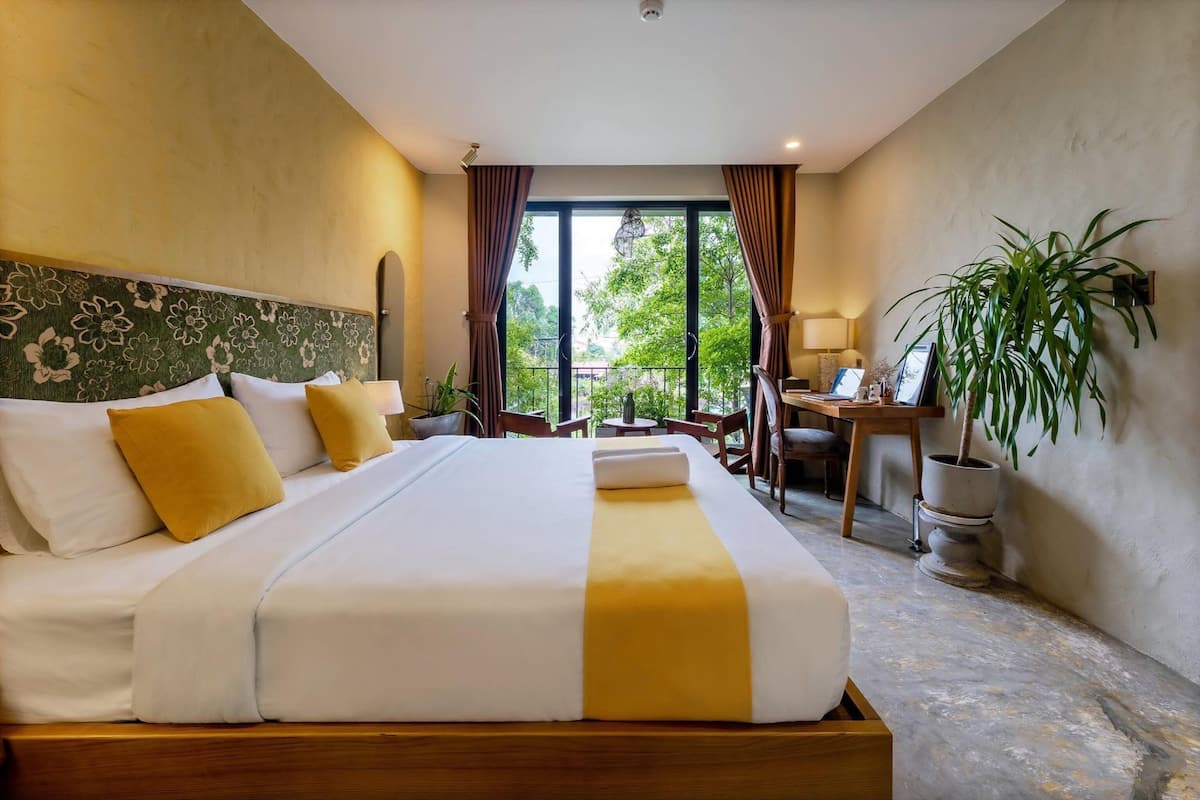 A hotel room with a large bed, a desk, a chair, and a potted plant.
