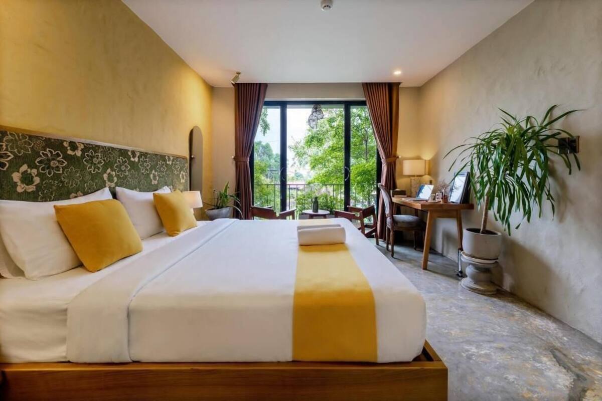A hotel room with a large bed, a desk, and a view of greenery outside.