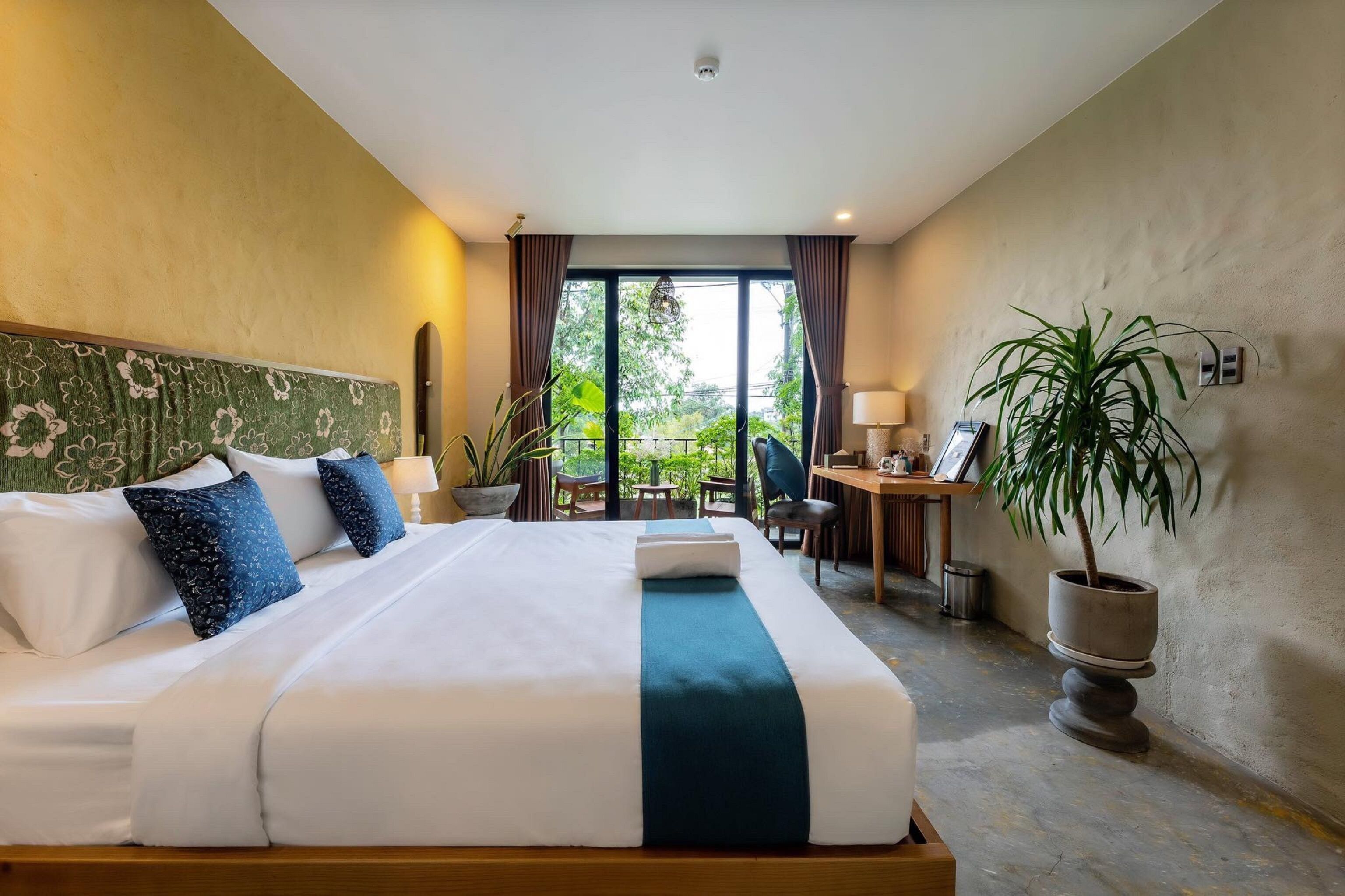 A hotel room with a large bed, a desk, and a potted plant.