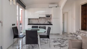 Une cuisine moderne avec des meubles blancs, un plan de travail en marbre et une table à manger en verre, accompagnée de chaises noires.