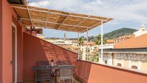 Un balcon avec une table et des chaises, une pergola et une vue sur les bâtiments et les collines.