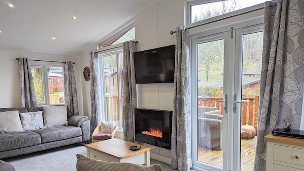 A modern living room with a grey sofa, a fireplace, and a large TV. - Fellhaven  -  a holiday lodge that sleeps 6 guests  in 3 bedrooms (Windermere)