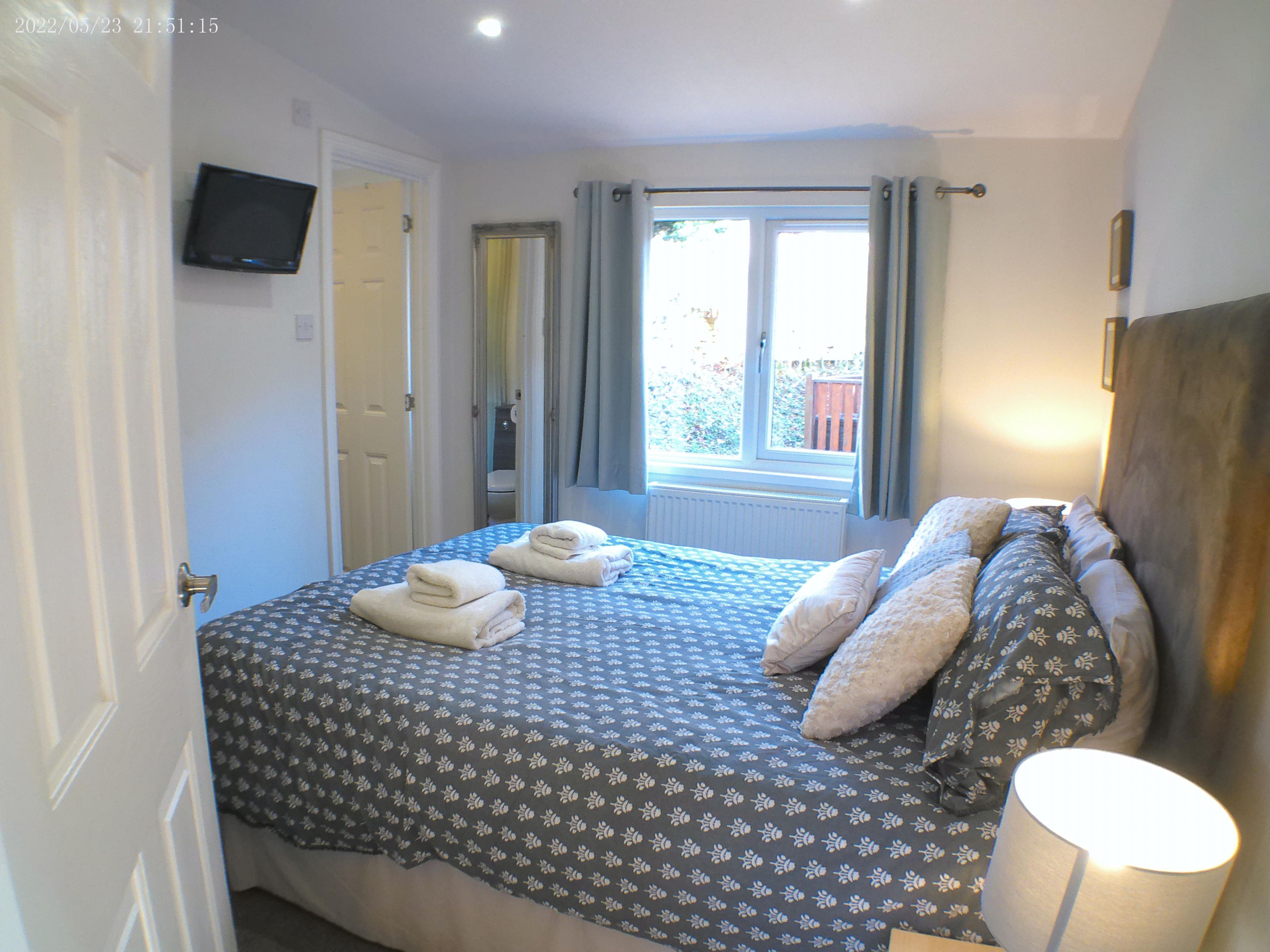 A bedroom with a bed, towels, a lamp, a TV, and a window with curtains.