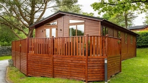 A wooden cabin with a fenced deck, surrounded by greenery. - Fellhaven  -  a holiday lodge that sleeps 6 guests  in 3 bedrooms (Windermere)