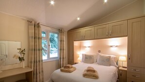 Une chambre à coucher comprenant un lit, des lampes de chevet, une table de chevet, un bureau avec une chaise, un miroir et une fenêtre avec des rideaux.