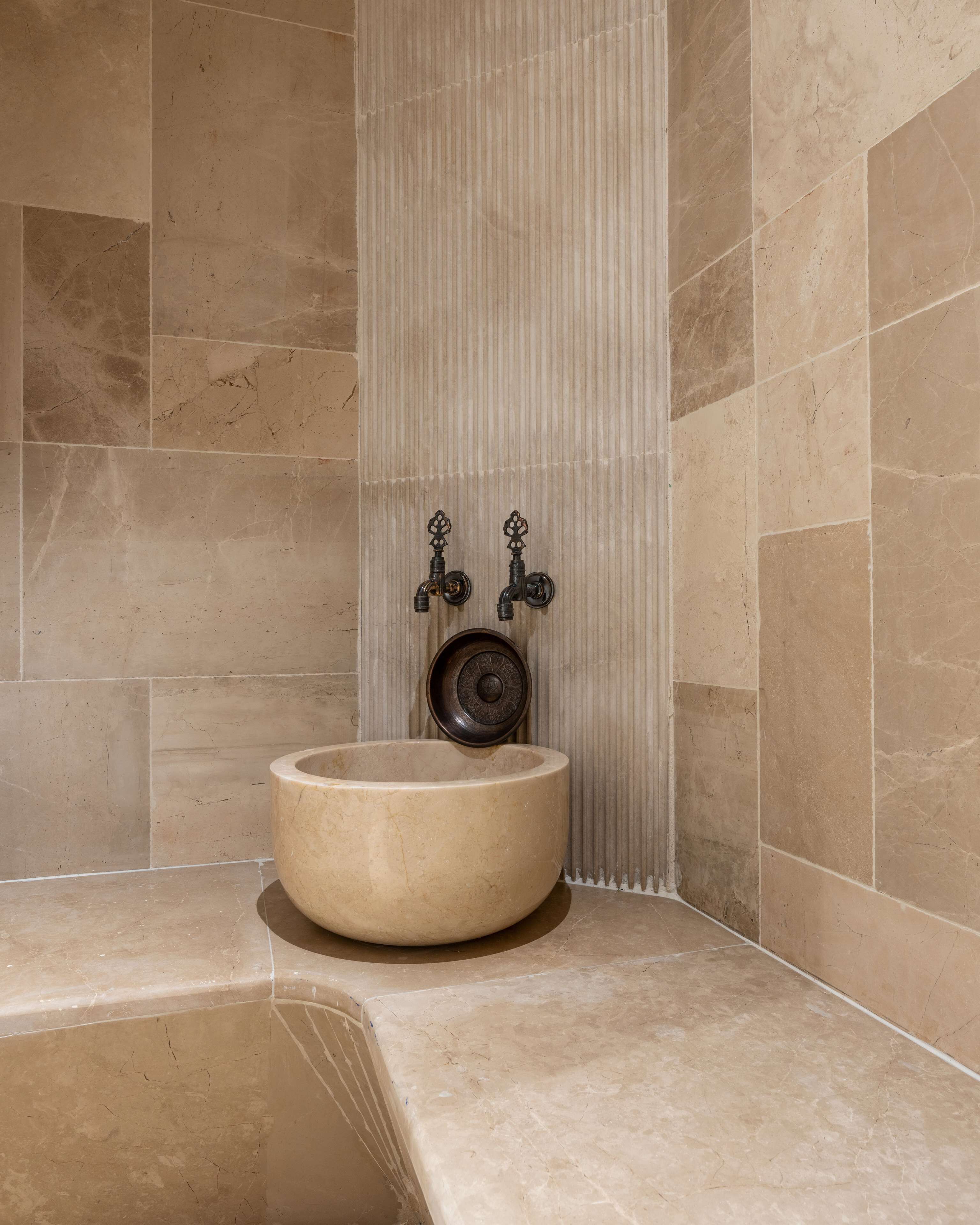 Un baño con un lavamanos grande y redondo de color beige y dos grifos negros con adornos.