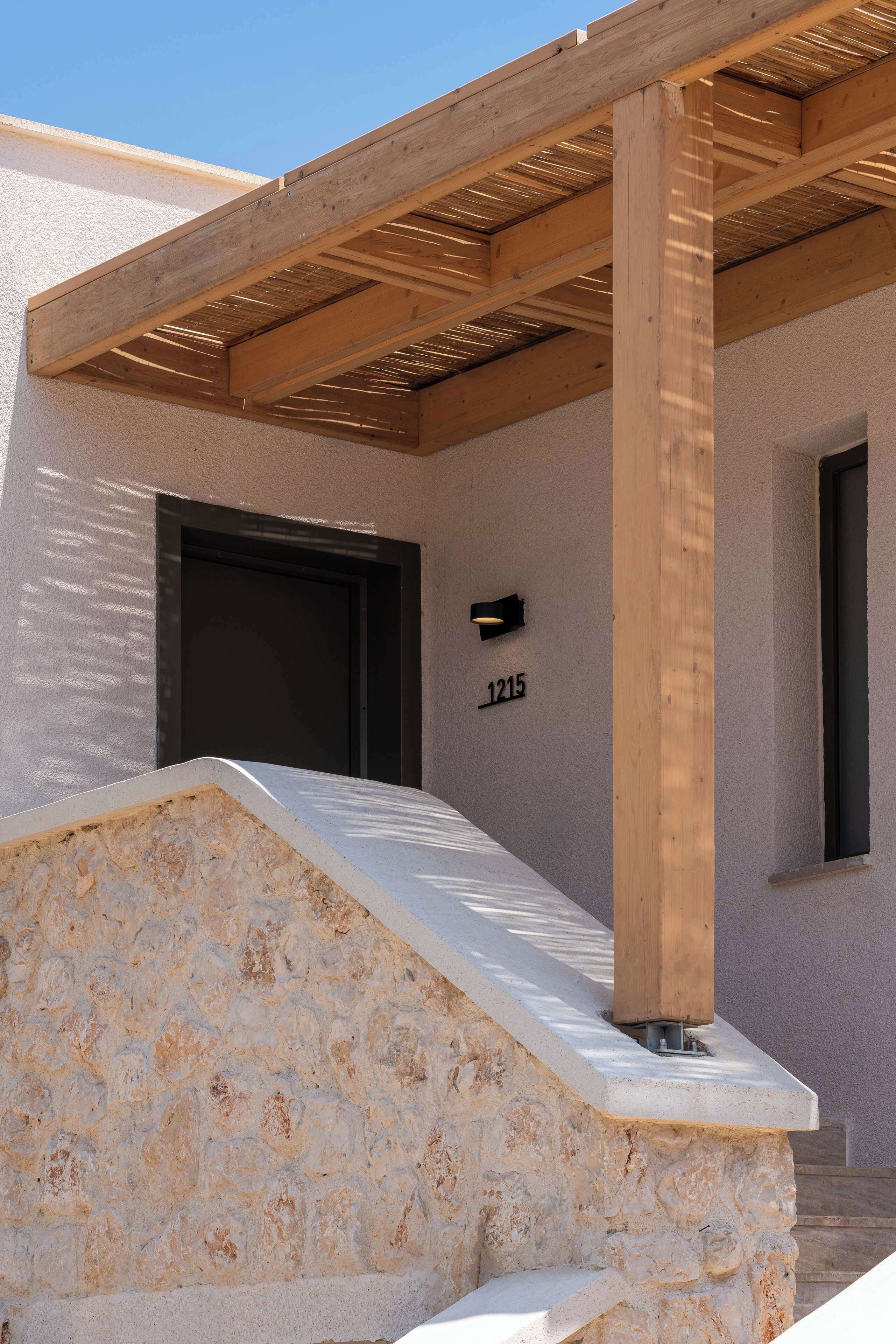 Un edificio de fachada de piedra, una pérgola de madera y una puerta con el número 1215.