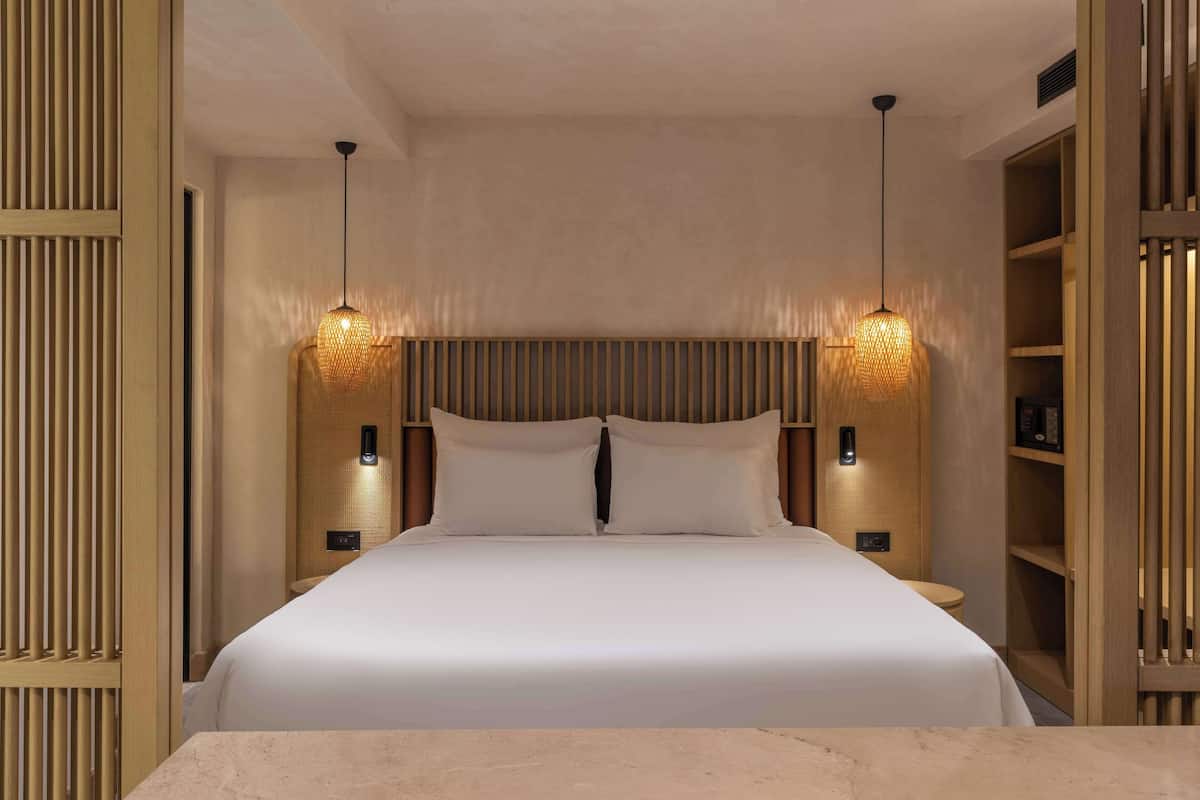 Una habitación de hotel moderna con una cama grande, dos lámparas de noche y estanterías de madera integradas.