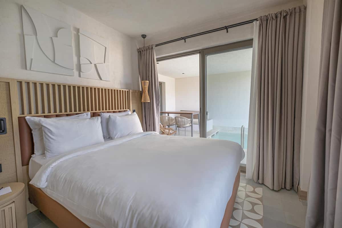 Habitación de hotel con una cama grande, cabecera de madera, una obra de arte en la pared, un balcón con puerta de vidrio y vista al mar.