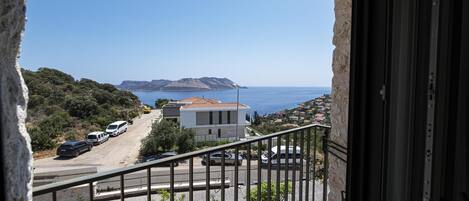 A balcony with a view of the sea, a parking area, and a building with a red roof.