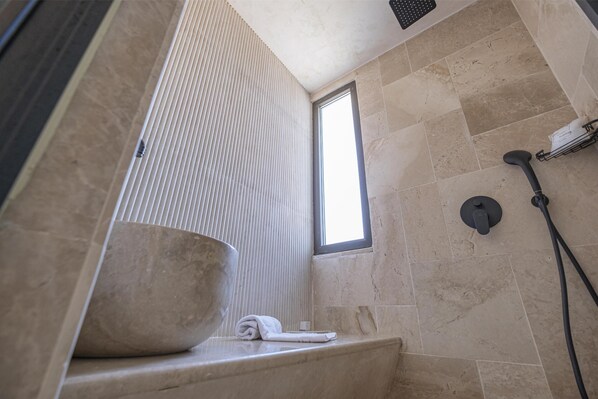 Un baño moderno con un lavamanos grande, una toalla, una ventana y un cabezal de ducha.