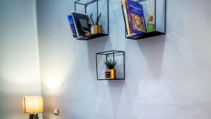 Un lit bien fait, avec une literie à motifs, une lampe de chevet et trois étagères murales ornées de livres et d’une plante.