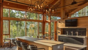 A modern kitchen with a large island, bar stools, and a TV mounted above the counter. - Ultra Luxury Mountain Retreat | Private Hot Tub + Firepits | Privacy | Summit Sky Ranch (Silverthorne)