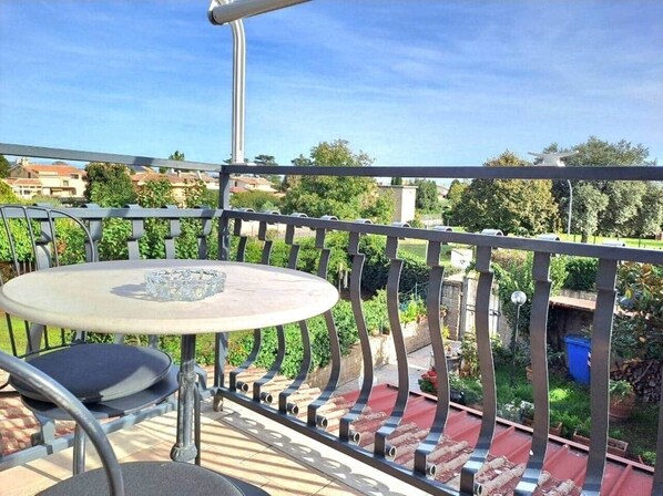 A balcony with a round table and chairs, surrounded by a metal railing.