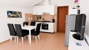 A compact kitchen with white cabinets, a dining table with chairs, a refrigerator, and a television.
