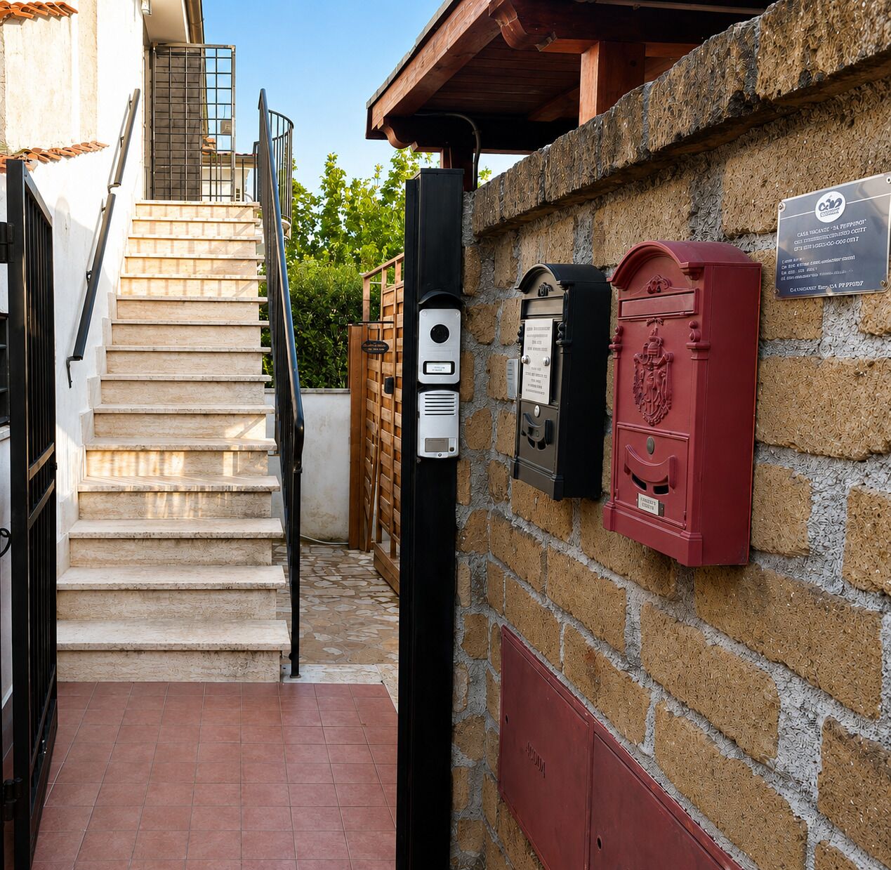 Un escalier menant à un bâtiment doté d’un mur en pierre, d’une boîte aux lettres et d’un portail en métal.