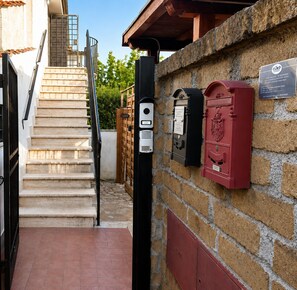 A staircase leading to a building with a stone wall, a mailbox, and a metal gate. - To complete (Anguillara Sabazia)