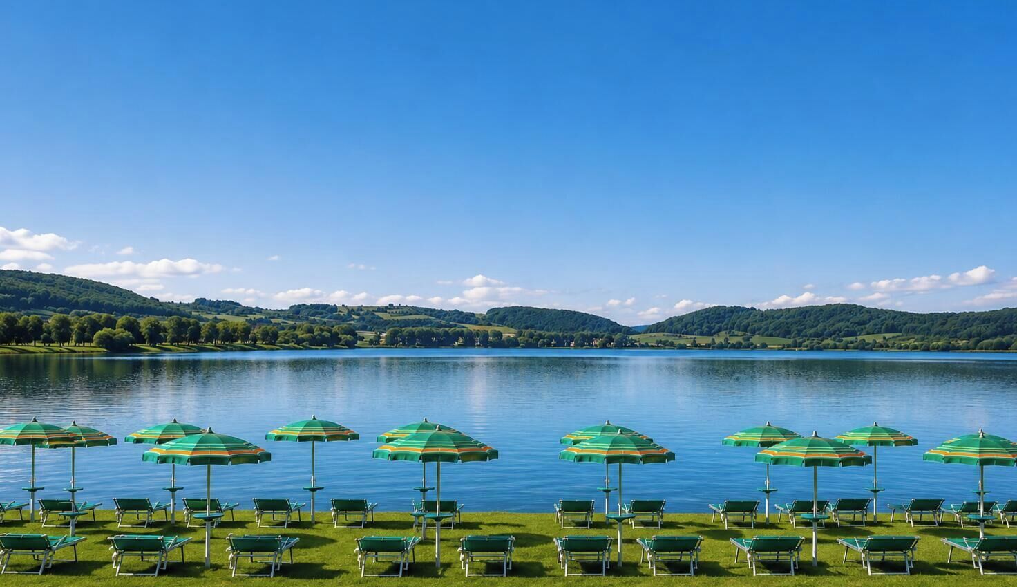 Vista del lago con hileras de sillas de césped verdes y sombrillas a rayas.
