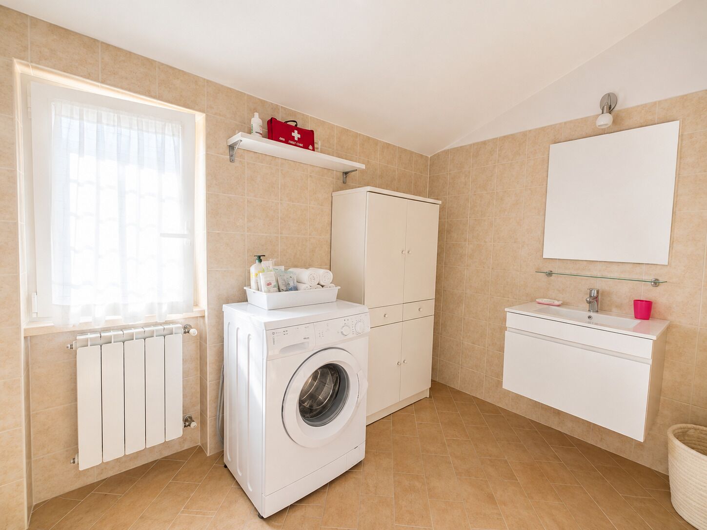 Ein Waschraum mit Waschmaschine, Wäscheständer, Schrank und Erste-Hilfe-Set auf einer Ablagefläche.