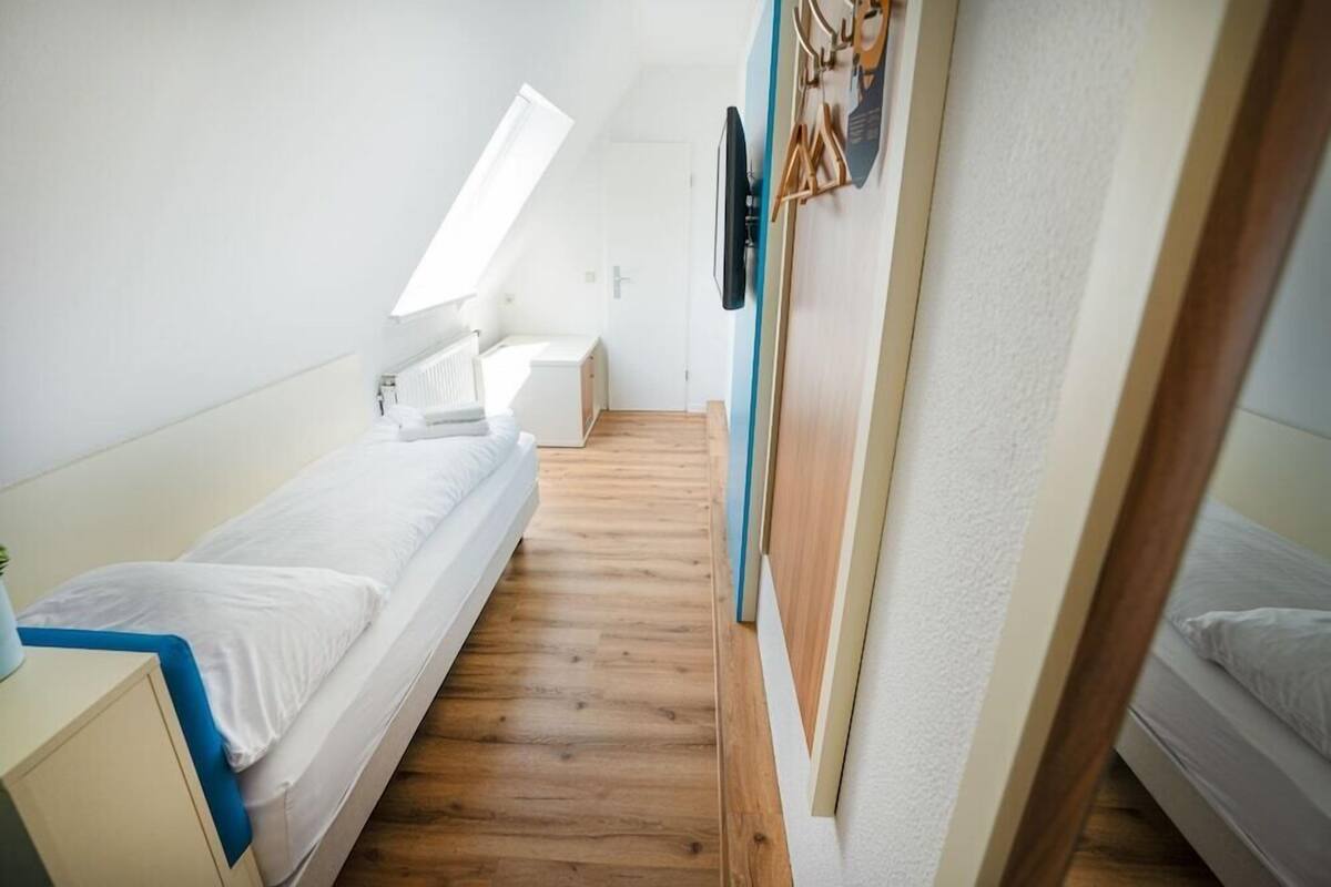 Une petite pièce lumineuse, avec un lit simple, un bureau, une chaise et une fenêtre.