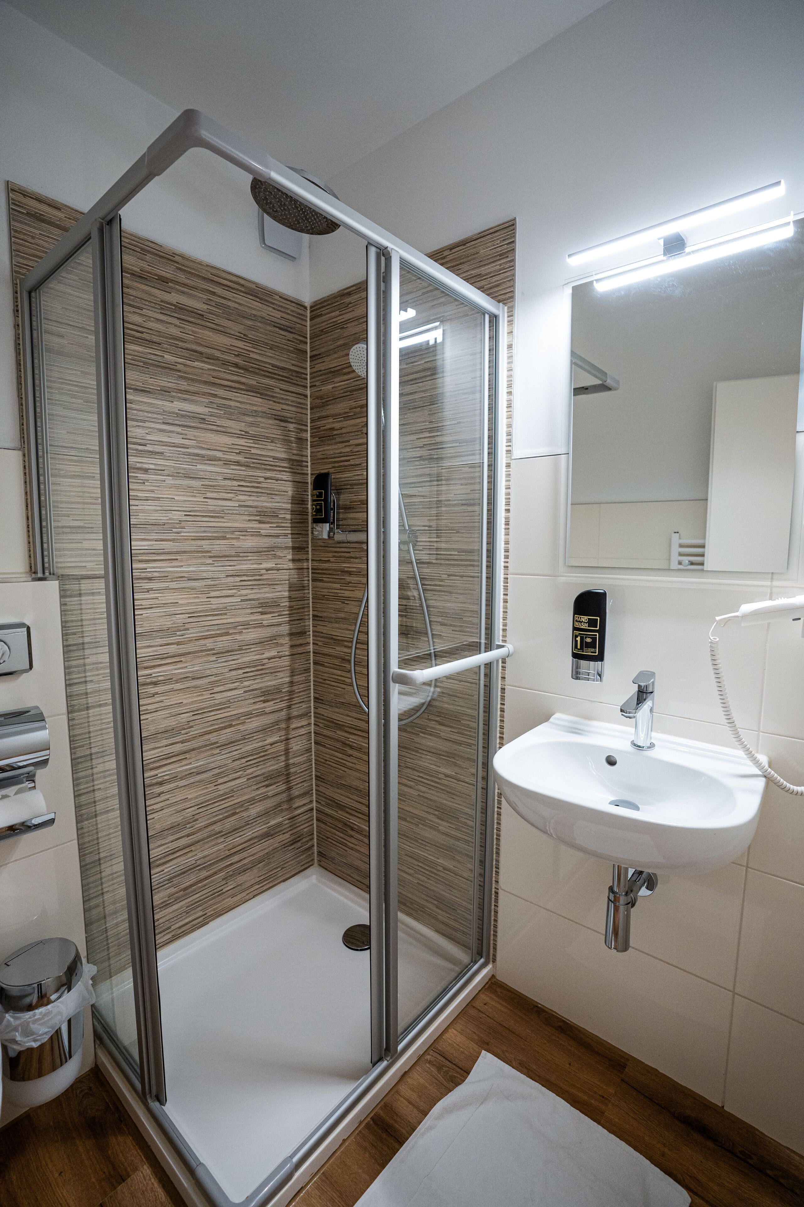 A modern bathroom with a glass-enclosed shower, a white sink, and a mirror above it.