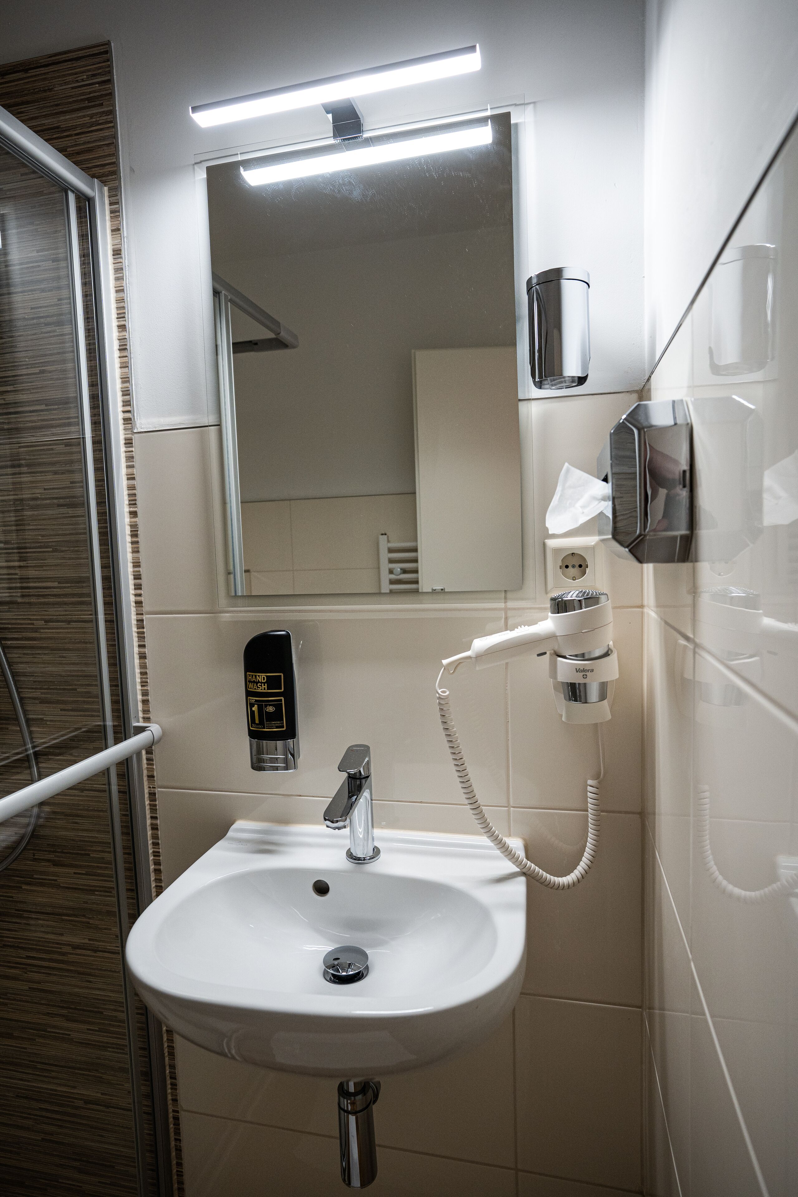 A bathroom with a white sink, a mirror, a towel dispenser, and a handheld showerhead.