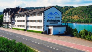 A hotel with a prominent sign, a view of a river, and a road in the foreground. - besttime Hotel Boppard (Boppard)