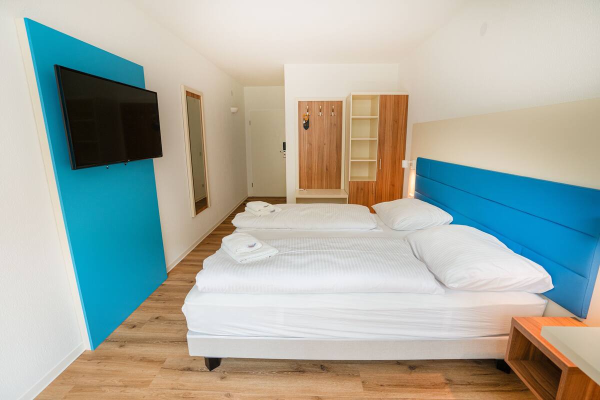Une chambre avec deux lits, un téléviseur fixé au mur et une armoire en bois.