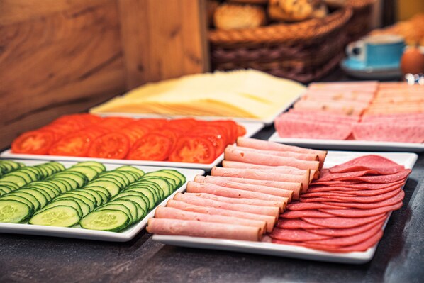 Un bufé con diversos alimentos, incluyendo pepinos en rodajas, tomates y diferentes tipos de carne.