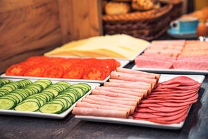 Un bufé con diversos alimentos, incluyendo pepinos en rodajas, tomates y diferentes tipos de carne.