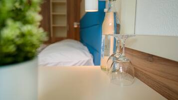 Ein Hotelzimmer mit einem Bett, einem Nachttisch mit einer Flasche und einem Glas, sowie einer Zimmerpflanze.