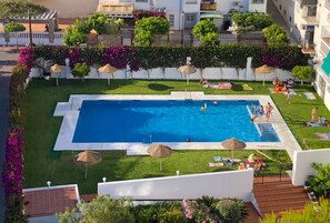Relax by the rectangular pool surrounded by lush greenery and white walls, with sun loungers and umbrellas providing shade.