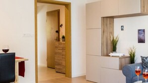 A modern living room with a grey sofa, a coffee table with a glass of red wine, and a wooden cabinet. - Ferienwohnung Eden Apartments (Friedrichshafen)