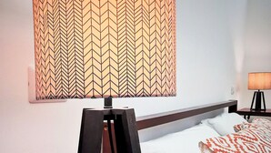 Ein Hotelzimmer mit einem Bett, einer Lampe mit sechseckigem Lampenschirm, einem Plüschtier und einer Visitenkarte auf dem Nachttisch.