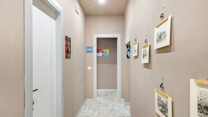 Ein schmaler Flur mit Fliesenboden, hellbeige Wänden und mehreren gerahmten Bildern an der rechten Wand.