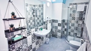 Ein Badezimmer mit Waschbecken, Spiegel, Pflanzenregalen, einer Dusche und gemusterten Fliesen.